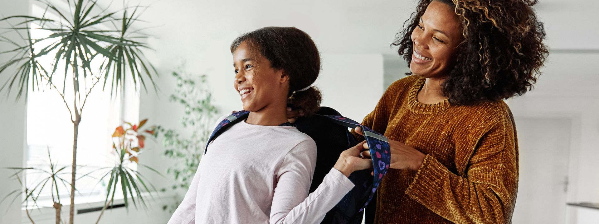 Mother helping daughter to get ready for school, helping her with backpack.